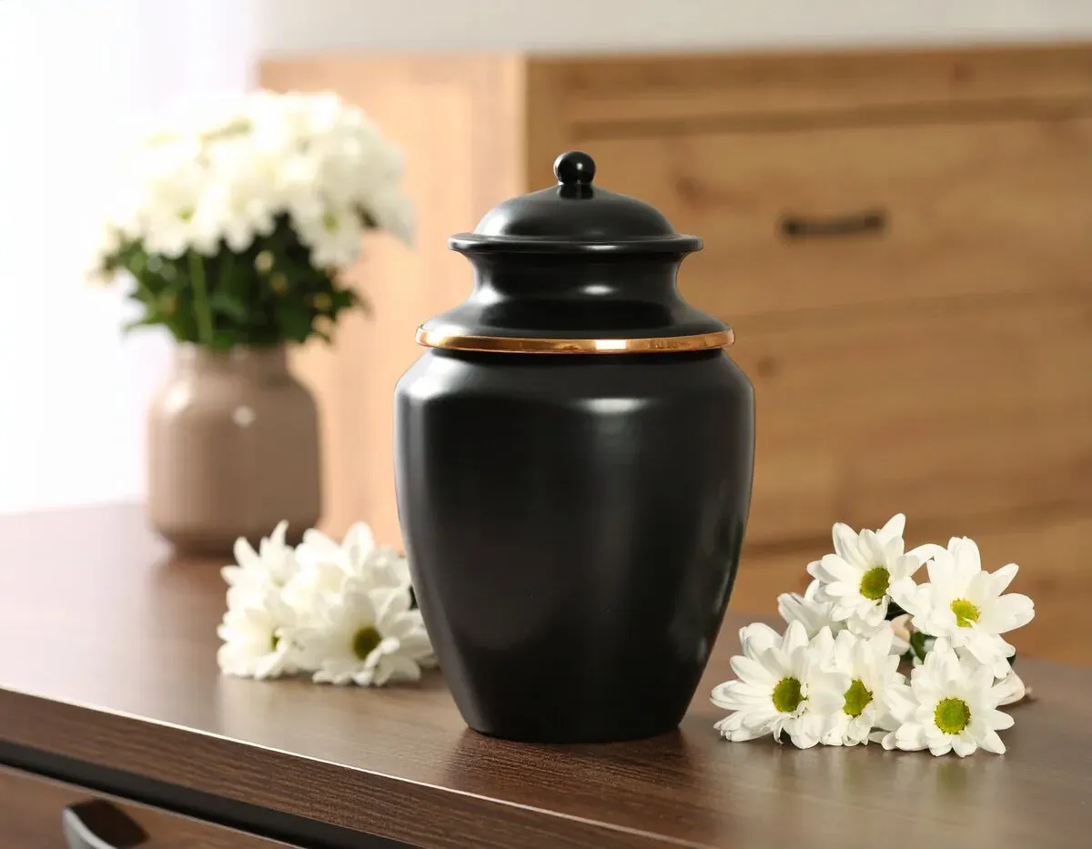 Urne funéraire noire posée sur une table auprès de fleurs blanches.